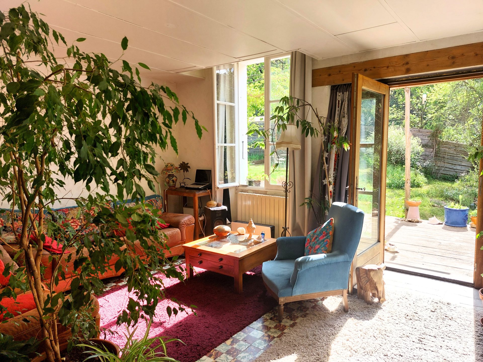 Salon : table en bois, armoires anciennes, plantes vertes, carreaux de ciment au sol