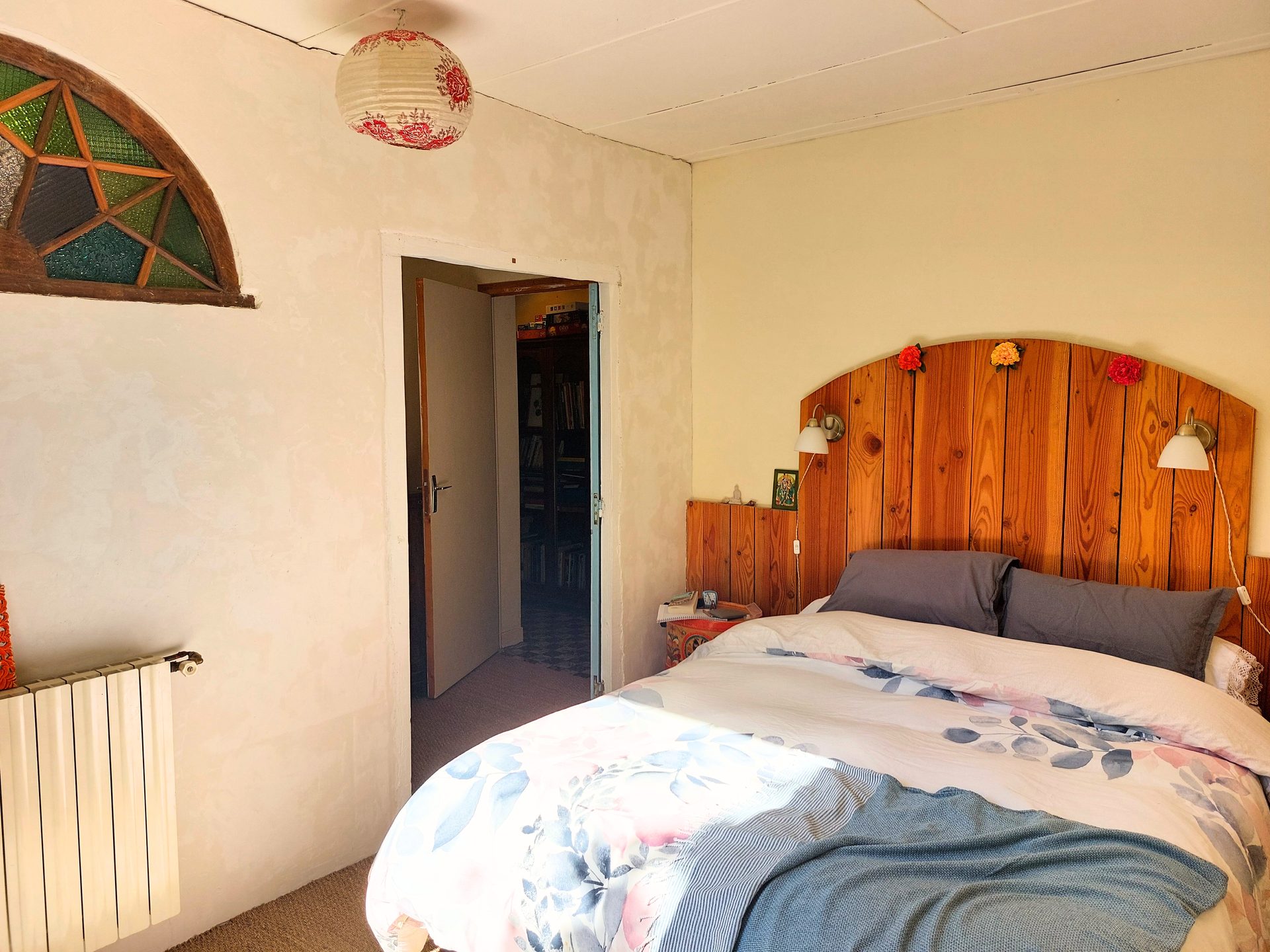 Chambre 1 : lit double, tête de lit en bois, vitrail ancien, mur enduit chaulé
